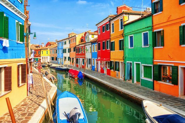 Un canale stretto con barche ormeggiate scorre tra file di case dai colori vivaci in una giornata di sole.