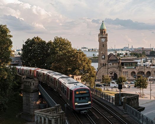 Un tren del metro de Hamburgo sobre un viaducto, junto a la torre del reloj de una estación histórica.
