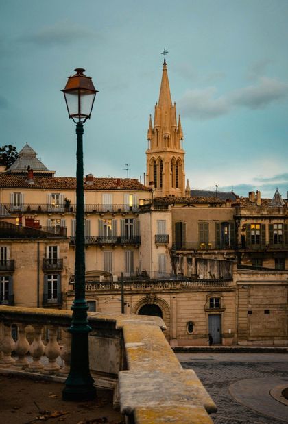 Der Kirchturm einer Kirche in Montpellier von einer Terrasse aus gesehen, mit einer schmiedeeisernen Laterne im Vordergrund.