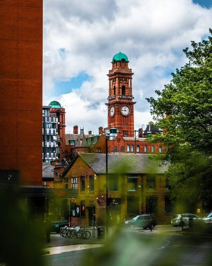 La torre del reloj de ladrillo rojo de un edificio victoriano de Mánchester, rodeada de árboles.