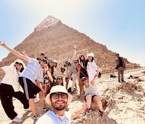Un voyage en groupe WeRoad posant et souriant pour un selfie devant une immense pyramide de pierre ancienne par une journée ensoleillée