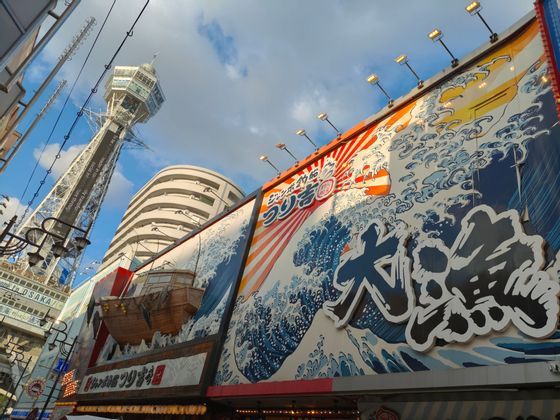 Vibrant commercial buildings featuring large wave artwork and a 3D boat facade near a tall observation tower.
