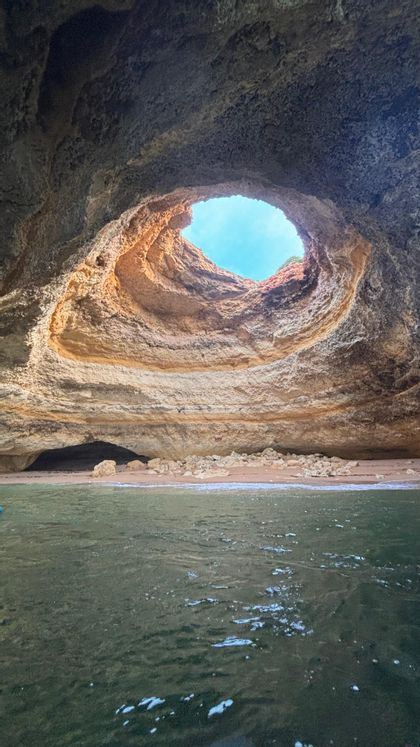 Une vue depuis l'eau à l'intérieur d'une grotte marine naturelle avec une ouverture circulaire dans le plafond révélant le ciel bleu