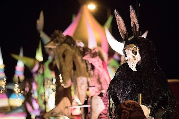 Une personne en costume sombre arborant un masque de crâne d'animal avec de longues oreilles lors d'un festival nocturne.