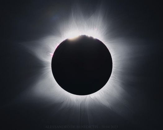 Un'eclissi solare totale che mostra la luminosa corona solare e le protuberanze solari rosa attorno alla silhouette oscura della luna.