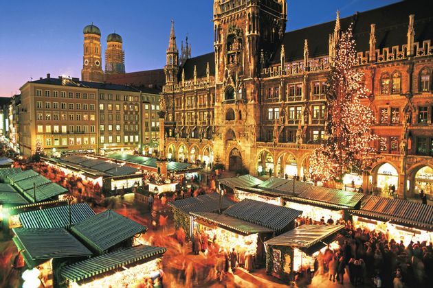 Un marché de Noël animé avec des stands illuminés et un grand sapin de Noël remplit une place de ville historique au crépuscule.