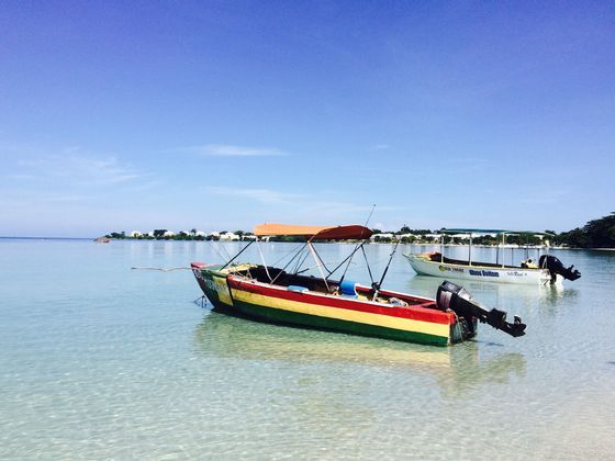 Un motoscafo a strisce rosse, gialle e verdi è ancorato in acqua limpida e bassa accanto a un'altra barca in una giornata di sole.