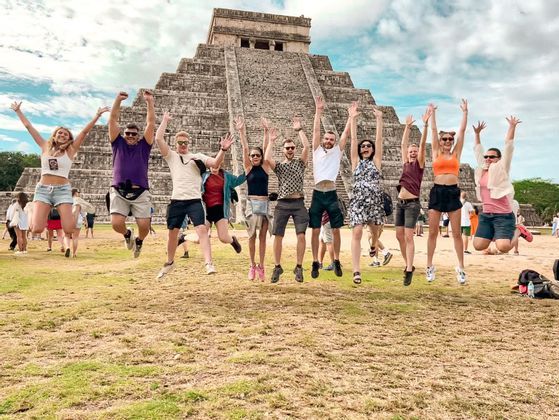 Eine WeRoad-Gruppenreise: Leute springen mit erhobenen Armen vor einer alten Steinpyramide in die Luft.