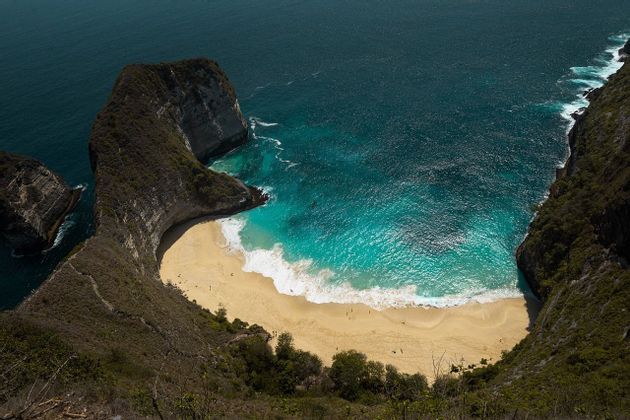 Une vue aérienne d'une crique isolée aux eaux turquoises et au sable doré, encerclée par des falaises rocheuses abruptes.