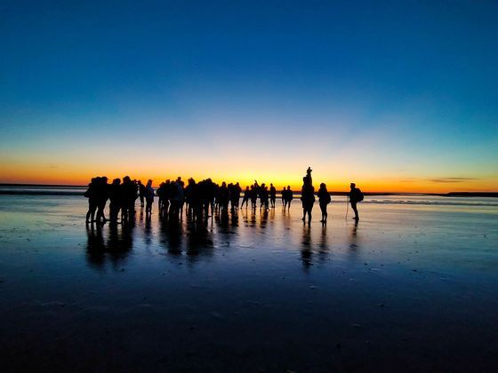 Un viaggio di gruppo WeRoad in silhouette contro un tramonto su una spiaggia bagnata, con i loro riflessi sulla sabbia.