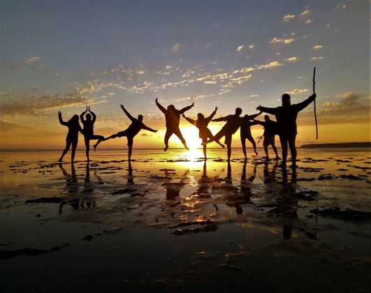 Un viaggio di gruppo WeRoad al tramonto, con i partecipanti in posa giocosa su una spiaggia bagnata e i loro riflessi nell'acqua.