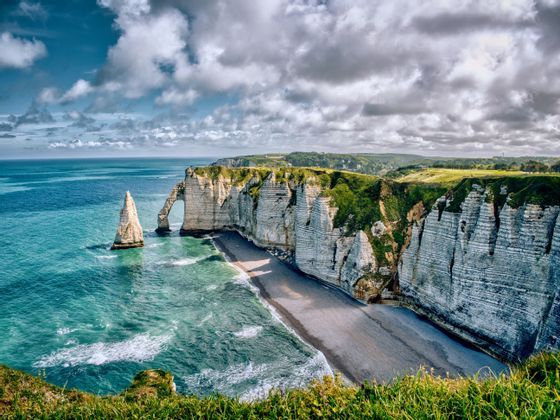 Scogliere di gesso bianche con un arco naturale e un faraglione, lungo una costa con acqua turchese sotto un cielo nuvoloso.