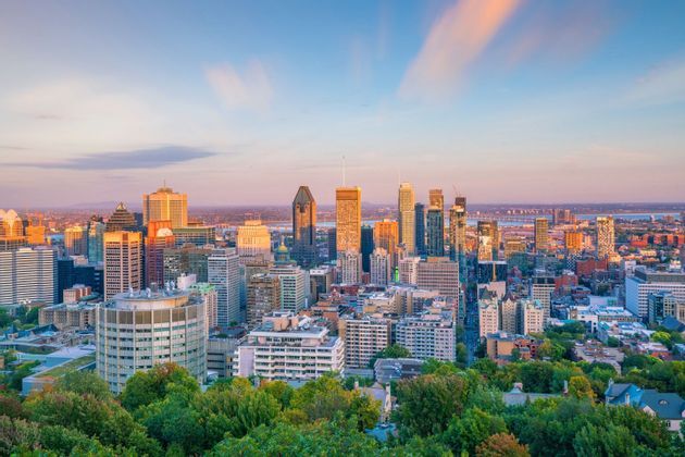 Un horizon urbain de gratte-ciel est illuminé par la lumière dorée du coucher de soleil, avec une forêt verte au premier plan.