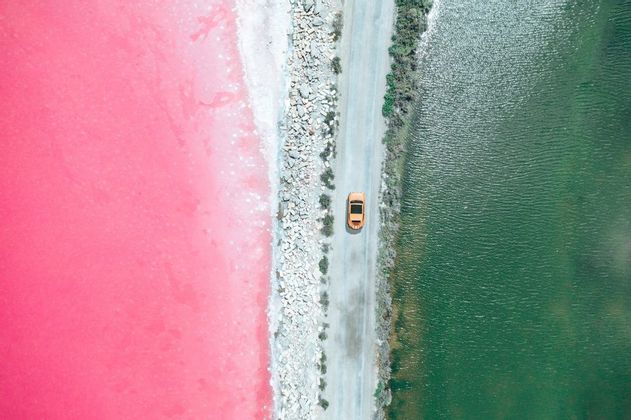 Una vista aerea di un'auto gialla che guida su una strada che separa un lago rosa vibrante da uno verde scuro.