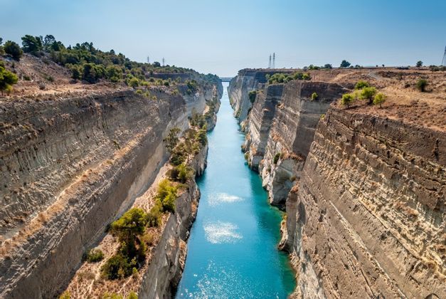 In una giornata di sole, un lungo e stretto canale dalle acque turchesi scorre tra ripide scogliere rocciose a strati.