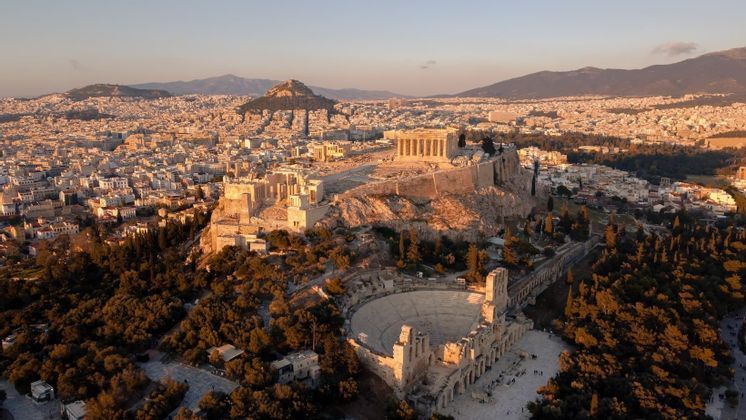 Veduta aerea dell'Acropoli e di un anfiteatro romano ad Atene, illuminati dalla luce dell'ora d'oro, che dominano il panorama cittadino.