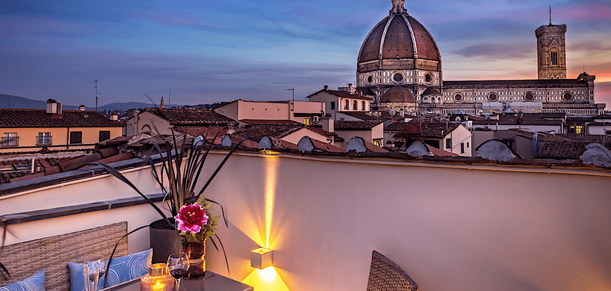 Terrazza arredata con vista sulla grande cupola di una cattedrale e sui tetti della città al tramonto.
