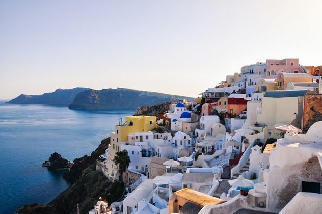 Un insieme di edifici bianchi e colorati con cupole blu su una scogliera che si affaccia sul mare calmo e blu.