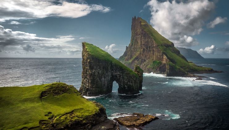 Due grandi faraglioni coperti d'erba verde, uno con un arco naturale, si ergono dall'oceano accanto a scogliere maestose.