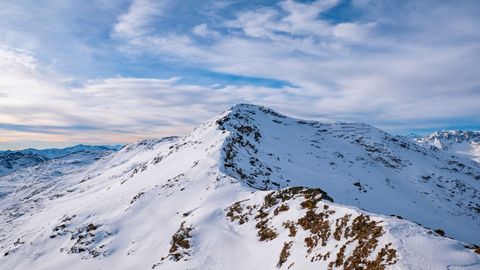 Una cima montuosa innevata con una cresta rocciosa sotto un cielo blu con nuvole sparse.