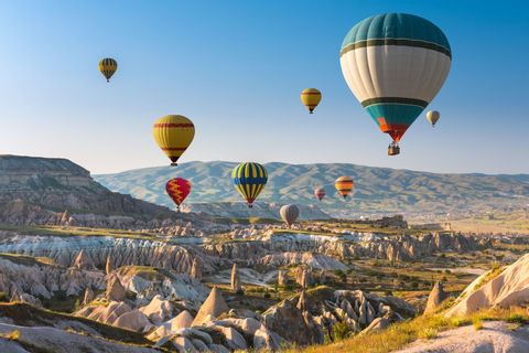 Mongolfiere colorate fluttuano su una valle rocciosa con formazioni a cono, sotto un cielo azzurro limpido.