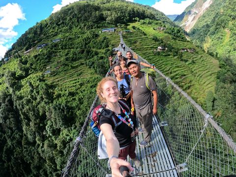Un grupo de WeRoad se hace una selfie al cruzar un largo puente colgante sobre un exuberante valle de montaña en terrazas.