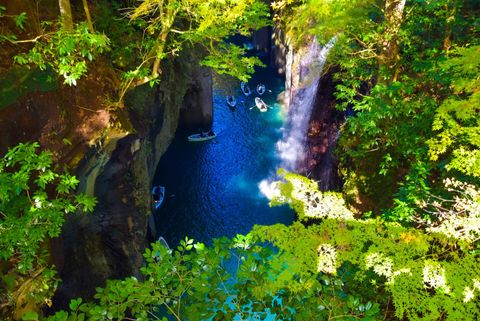 Veduta aerea di un viaggio di gruppo WeRoad che pagaia in barca in una gola stretta con acqua blu vibrante e una cascata.