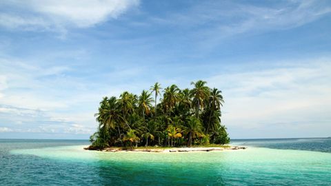 Una pequeña isla tropical cubierta de palmeras, rodeada de aguas turquesas y cristalinas bajo un cielo azul con nubes ligeras.