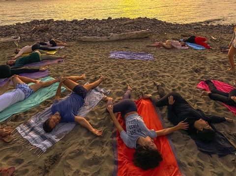 Un gruppo WeRoad in viaggio si rilassa sugli asciugamani su una spiaggia sabbiosa, facendo stretching al tramonto.