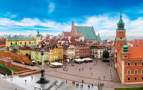 Vue plongeante sur une place de ville historique avec des bâtiments colorés, une colonne imposante et une tour horloge sous un ciel bleu éclatant.