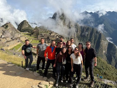 Un grupo de WeRoad posa para una foto con ruinas de piedra antiguas y montañas cubiertas de nubes al fondo.