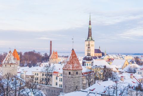 La silhouette hivernale d'une ville historique, avec ses toits enneigés, ses tours de pierre aux toits rouges et un haut clocher d'église.