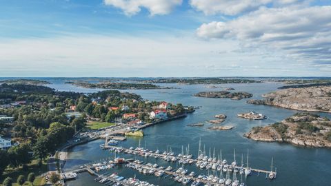 Eine Luftaufnahme einer Marina voller Boote an einer Küste mit felsigen Inseln unter blauem, bewölktem Himmel.