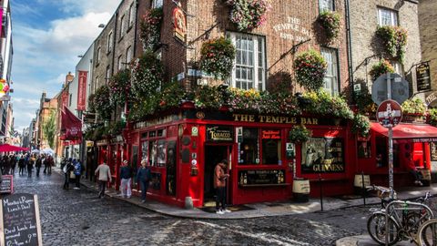Das Temple Bar Pub mit seiner roten Fassade und hängenden Blumenkörben an einer gepflasterten Straßenecke in einer Stadt.