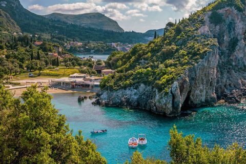 Boote schwimmen auf türkisfarbenem Wasser in einer Bucht, umgeben von üppig grünen Klippen und einem kleinen Stranddorf.