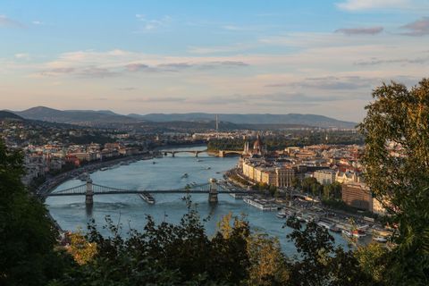 Una veduta aerea di una città attraversata da un grande fiume, solcato da diversi ponti, con colline sullo sfondo sotto un cielo blu.