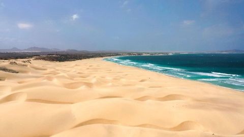 Vastas dunas de arena dorada descienden hasta el encuentro de las olas turquesas del océano a lo largo de una extensa costa.
