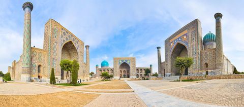 Vista panorámica de edificios históricos ornamentados con minaretes y azulejos azules, rodeando una gran plaza abierta bajo un cielo azul.