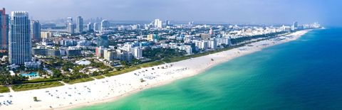 Una vista aérea de una extensa ciudad costera con rascacielos junto a una larga playa de arena blanca y océano turquesa.