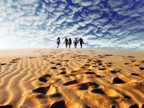 Un grupo de WeRoad camina por una inmensa duna de arena, dejando huellas en la arena bajo un cielo azul nublado.