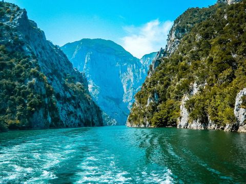 View from a boat on a turquoise river winding through a steep, forested mountain canyon under a blue sky.