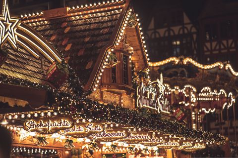 Un puesto de mercado navideño de madera decorado con luces festivas, letreros y una gran estrella iluminada en su tejado por la noche.