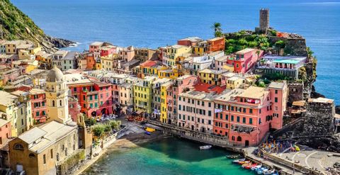 Vista panorámica de un pueblo costero con edificios coloridos, apiñados en un acantilado que domina un puerto turquesa y el mar azul.
