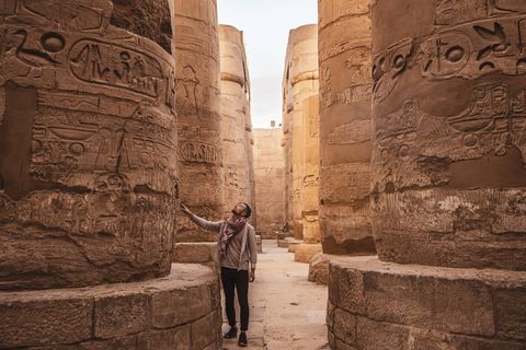 A man stands in an ancient temple hall, looking up at the hieroglyphs carved into the massive stone columns.