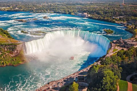 Una vista aérea de una cascada masiva en forma de herradura con un barco turístico navegando las aguas brumosas en su base.