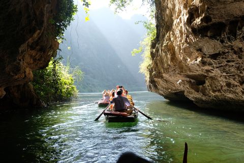 Un viaje en grupo de WeRoad rema en botes por un río a través de un desfiladero soleado entre grandes acantilados rocosos.