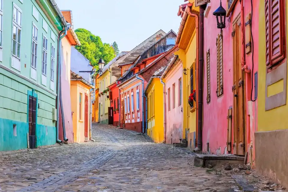Una estrecha calle empedrada y vacía serpentea cuesta arriba, flanqueada por edificios históricos de colores vivos bajo un cielo despejado.
