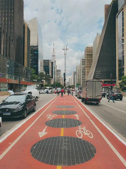 Una pista ciclabile rossa con simboli bianchi di bicicletta si snoda al centro di un ampio viale cittadino fiancheggiato da grattacieli.