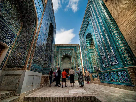 Un gruppo WeRoad si trova in uno stretto passaggio, ammirando imponenti edifici ricoperti di intricate piastrelle a mosaico blu sotto un cielo parzialmente nuvoloso.