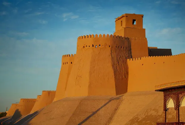 Una grande fortezza color sabbia con torri e mura fortificate si crogiola al caldo sole sotto un cielo azzurro e limpido.